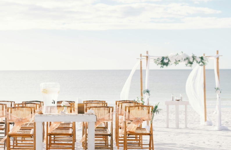 Montaje de ceremonia para una boda destino en la playa de Almería con altar decorado, sillas de madera y vistas al mar al atardecer.